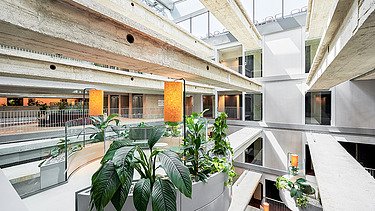 Helles Innenatrium des RAIQA-Quartiers mit begrünten Bereichen, offenen Galerien und moderner Innenarchitektur.