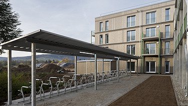Fotografie vícepodlažní budovy postavené metodami sériové dřevostavby, s krytým parkovištěm pro jízdní kola