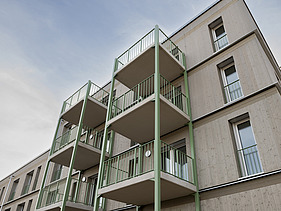 Photograph of a multi-storey residential building constructed using a standardised timber-frame method, featuring green balcony structures