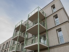 Photograph of a multi-storey residential building constructed using a standardised timber-frame method, featuring green balcony structures