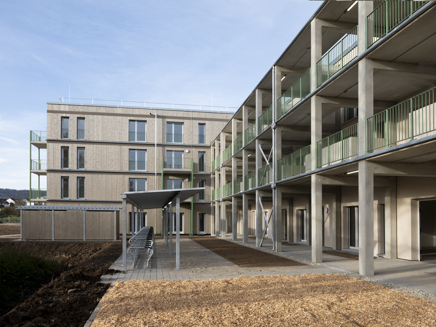 Photograph of a multi-storey building constructed using serial timber construction, featuring a covered cycle parking area