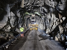 A tunnel construction site with a tunnel boring machine and workers in the rock tunnel.