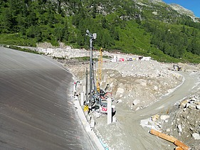 Construction site of a pumped-storage power station in an alpine landscape, with access roads, a drilling rig and construction vehicles