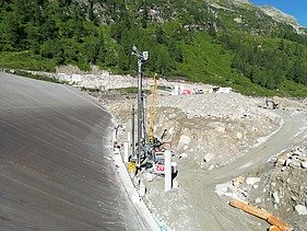 Construction site of a pumped-storage power station in an alpine landscape, with access roads, a drilling rig and construction vehicles