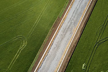 Aufnahme aus der Vogelperspektive: Straße, die durch ein Feld verläuft