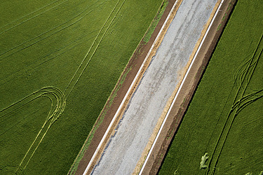 Aufnahme aus der Vogelperspektive: Straße, die durch ein Feld verläuft