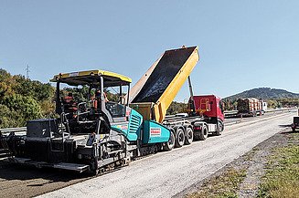 Road paver and truck doing cold recycling work on a highway under a blue sky.