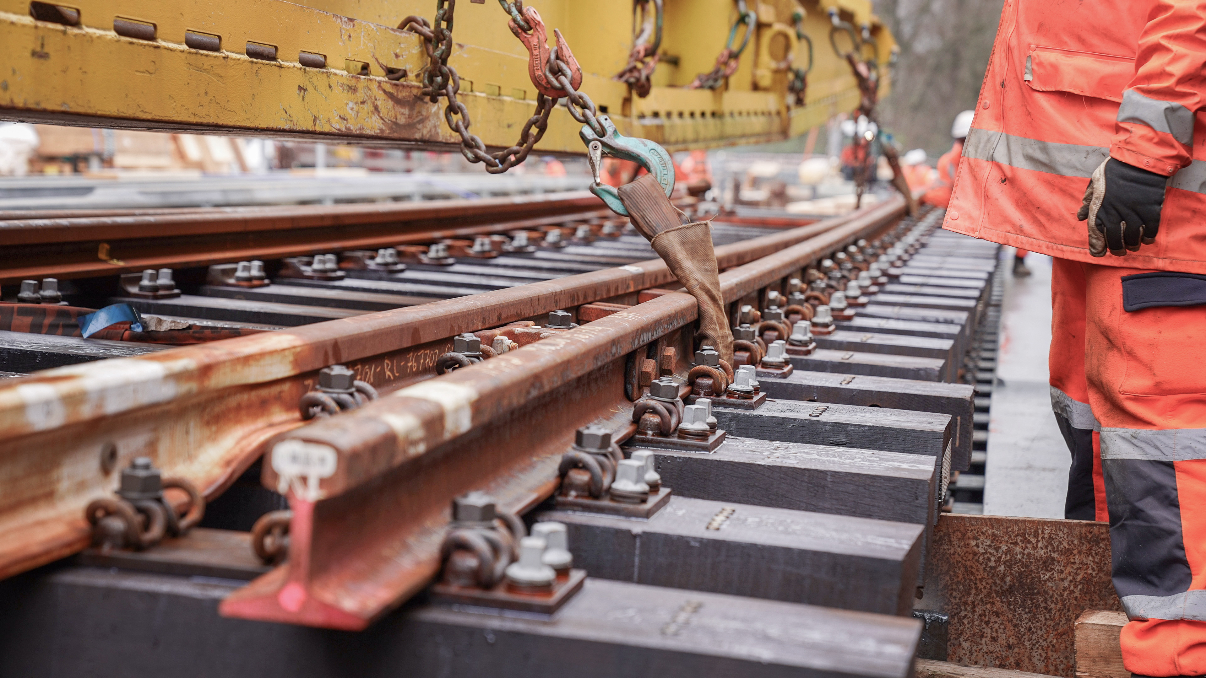 Close-up of track works: rails, sleepers and fastenings are being fitted using a crane and tools