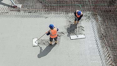 Beton o obniżonej emisji CO2 jest wylewany przez dwóch pracowników.