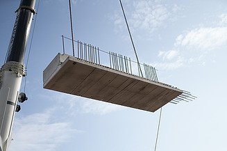 Jeřáb zvedá prefabrikovaný betonový díl s výztuží