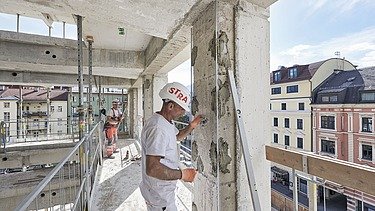 Bauarbeiten im RAIQA-Quartier Innsbruck mit Mitarbeitenden auf einer Rohbauetage und Blick auf die umliegende Stadt.