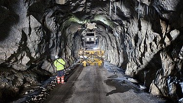 Tunnelbaustelle mit Tunnelbohrgerät und Mitarbeitenden im Felsstollen.