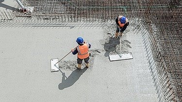 Beton o obniżonej emisji CO2 jest wylewany przez dwóch pracowników.