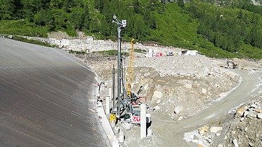 Baustelle eines Pumpspeicherkraftwerks in alpiner Landschaft mit Zufahrtsstraßen, Bohrgerät und Baustellenfahrzeugen