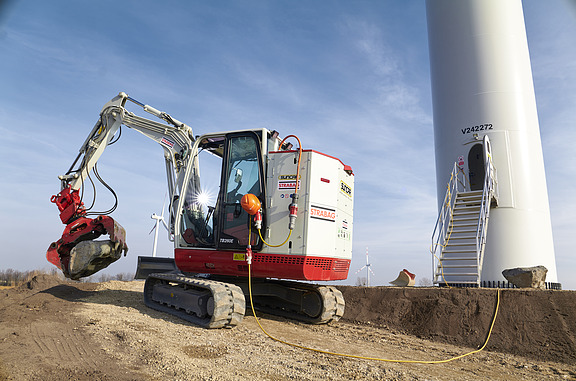 Photo of an electric excavator using green electricity from a wind turbine