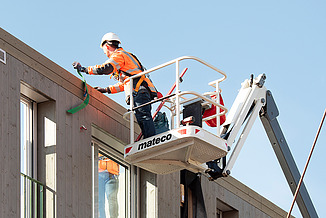 Fotografie stavebních dělníků při instalaci dřevěných hybridních vnějších stěn