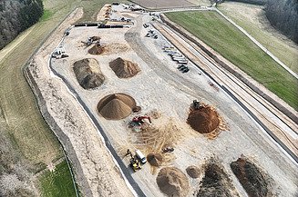 Letecký pohľad na stavenisko s hromadami zeminy, bagrami a nákladnými autami pre projekt elektrického vedenia